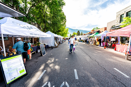 Aspen, USA - July 6, 2019: Vendors selling produce meat at stall stand in farmers market with people walking in outdoor summer street