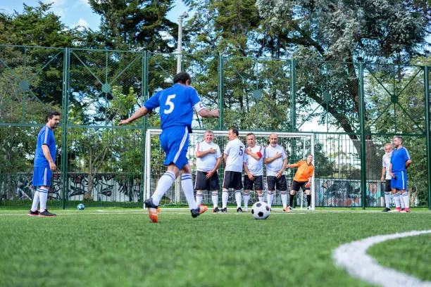 Older footballer of Latin ethnicity between 50-60 years old is about to charge a free kick so that the team manages to miss a goal