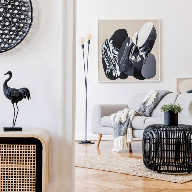 Modern scandinavian interior design of open space with stylish wooden commode, gray sofa, rattan table, plant, tropical leaf and elegant personal accessories. Stylish home decor Template. Home staging