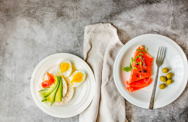 Rice crispy cakes with avocado and fresh salted salmon fillet with eggs on a gray marble background. Top view. Space for text. High protein and low carb meal. salmón de pescado rojo ahumado con aceitunas, huevos de codorniz, nueces y pasteles crujientes de arroz con aguacate sobre un fondo gris. vista superior. rústico. productos con omega-3 buenos para un cabello y una piel saludables. espacio para texto.
