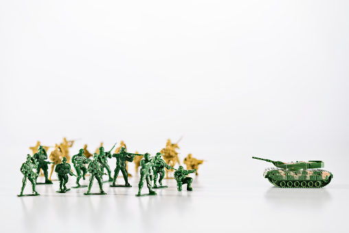 Battle, small army of toy soldiers are standing against the tank, selective focus, white background.