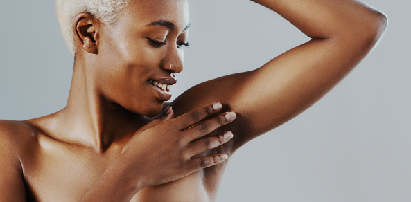 Cropped shot of an attractive young woman standing alone and touching her underarm against a gray background in the studio