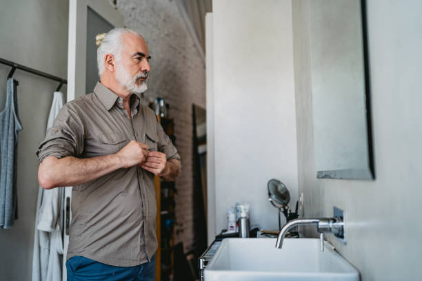 Senior man dressing up Senior handsome man dressing up in bathroom. buttoning stock pictures, royalty-free photos & images