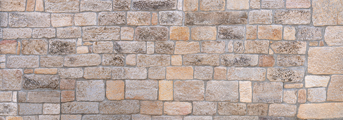 Panorama of a bright, pastel-colored, old, partly weathered stone wall made of different stones