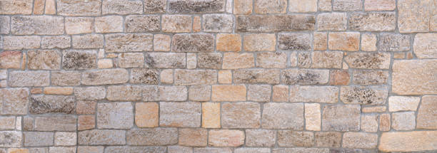 Panorama of a bright, old, partly weathered stone wall Panorama of a bright, pastel-colored, old, partly weathered stone wall made of different stones roughhewn stock pictures, royalty-free photos & images