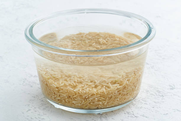 Soaking brown rice cereal in water to ferment cereals and neutralize phytic acid. Large glass bowl with grains flooded with water. Side view, close up, white background Soaking brown rice cereal in a water to ferment cereals and neutralize phytic acid. Large glass bowl with grains flooded with water. Side view, close up, white background drenched stock pictures, royalty-free photos & images