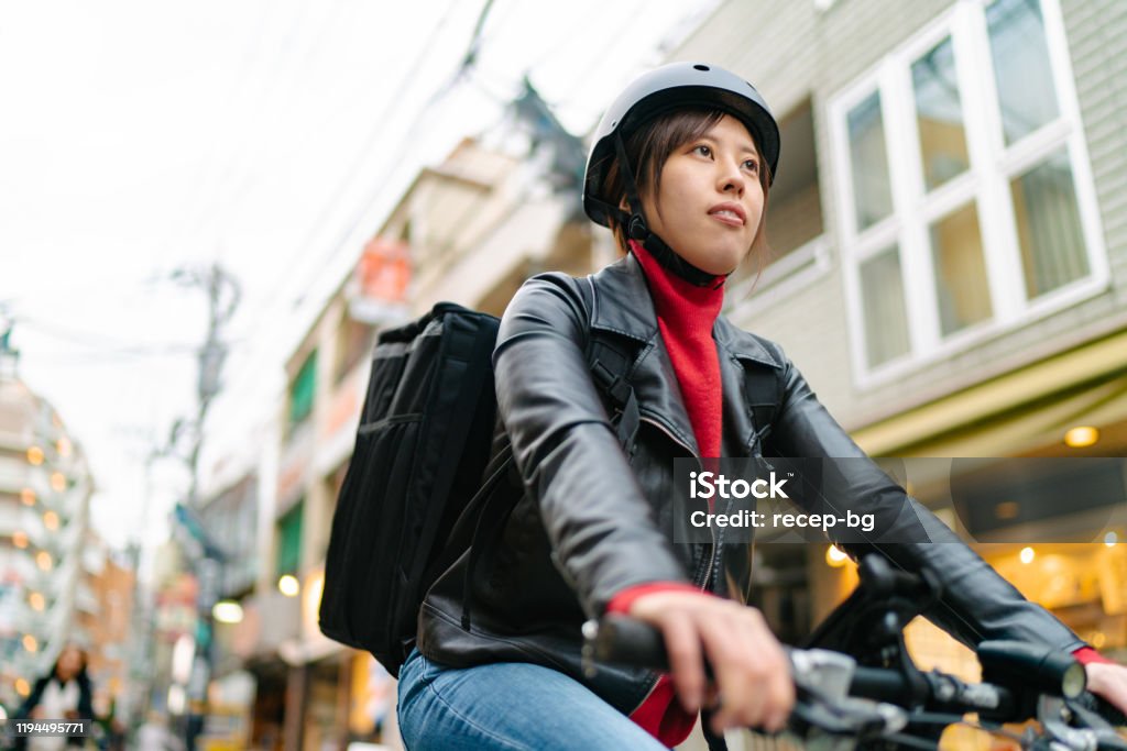 Young woman riding on bicycle for food delivery A young woman is riding on a bicycle in the street for food delivery. Cycling Stock Photo