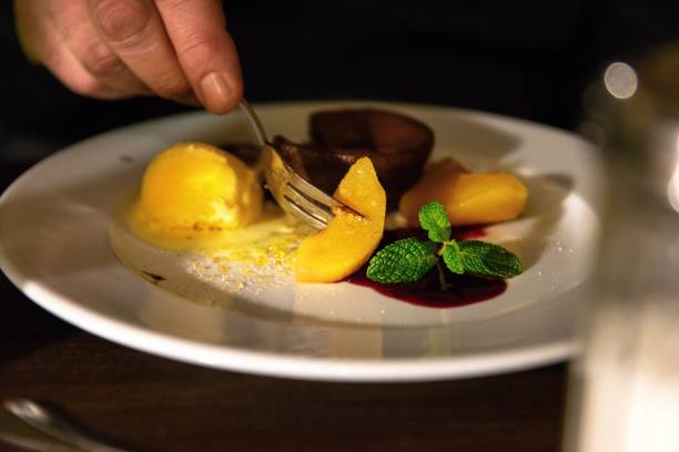istock Dessert with peaches, vanilla ice cream and chocolate cake, hand with fork. 1194498532