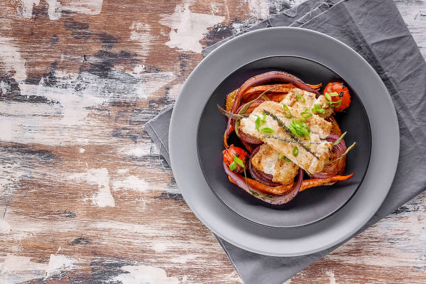 istock Top view appetizing cod filet with red onion and herbs: sage, rosemary and thyme, baked potatoes and carrots on a side dish in a gray plate on a gray napkin. Tasty and healthy sea fish. Copy space 1194498626
