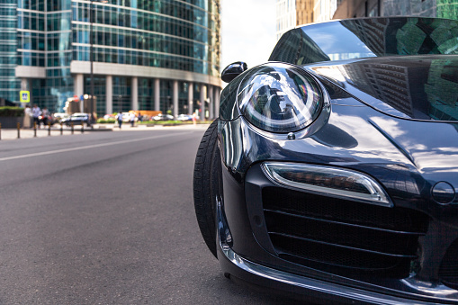 Russia Moscow 2019-06-17 Closeup headlights of new shiny luxury dark blue sports car Porsche 911 parked on the street, front bottom view, sky reflection on bonnet, bumper