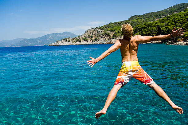 A young man jumping into the blue waters of the sea stock photo