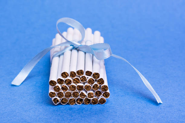 istock A stack of new thin cigarettes is tied with a blue ribbon with a bow lying on a blue background. The danger of smoking for women. Fatal addiction. 1194503759