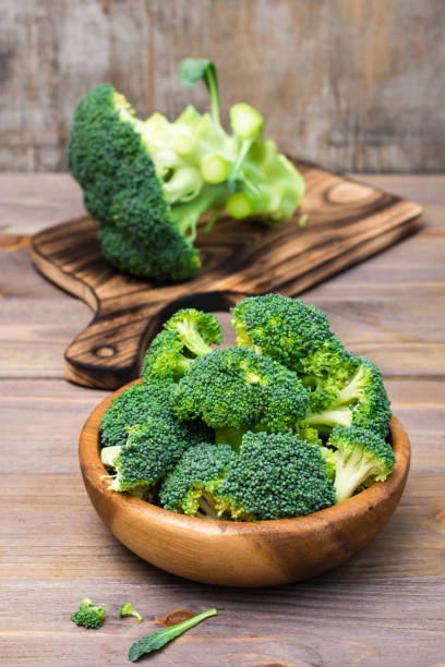 ready to eat fresh raw broccoli is divided into inflorescences in a wooden plate and on a cutting board  on a wooden table. healthy lifestyle, nutrition and zero waste concept - cauliflower vegetable portion cabbage imagens e fotografias de stock