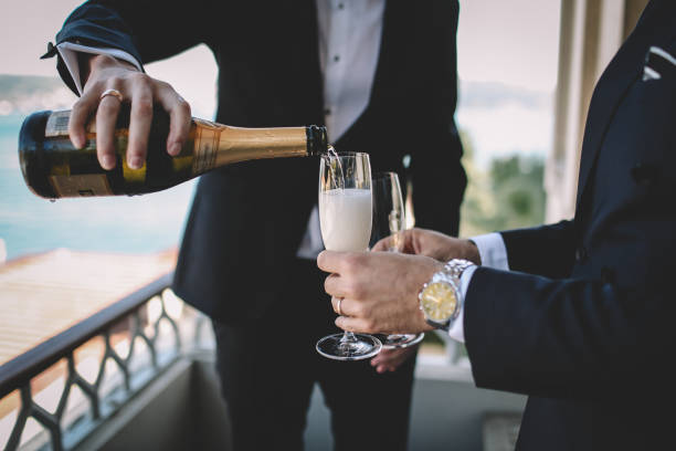 A woman is pouring a class of champagne outdoors in the sunshine.  Champagne, celebration, elegance, party, vacation, recreational pursuit, fun, enjoyment.