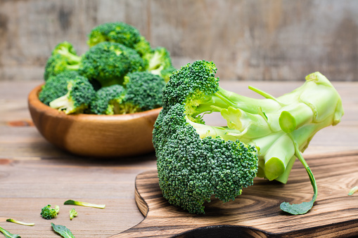 Ready to eat fresh uncooked broccoli on a cutting board and divided into inflorescences in a wooden plate behind on a wooden table. Healthy lifestyle, nutrition and zero waste concept