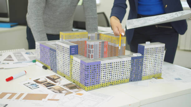 istock Engineer with scheme in hand shows models of houses and explain something to workmate 1194505644