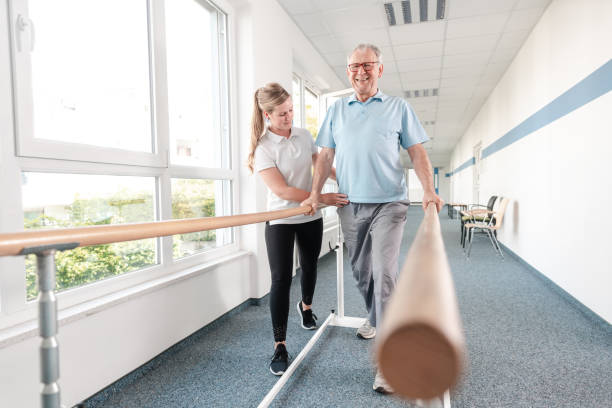 Senior Patient and physical therapist in rehabilitation walking exercises Senior Patient and physical therapist in rehabilitation walking exercises, she is helping him along the bars gymnastics bar photos stock pictures, royalty-free photos & images