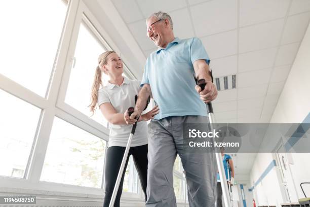 Seniors In Rehabilitation Learning How To Walk With Crutches Stock Photo - Download Image Now