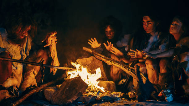 neandertaler oder homo sapiens familie kochen tierfleisch über bonfire und dann essen. stamm der prähistorischen jäger-sammler tragen tierhäute essen in einer dunklen beängstigend höhle in der nacht - steinzeit stock-fotos und bilder