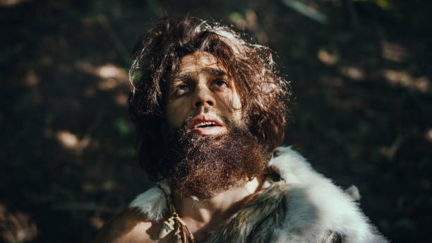 ritratto di cavernicolo primordiale che indossa la pelle animale alza le mani al cielo guardando il sole, avendo esperienza religiosa pagana. neanderthal preistorico credendo e pregando dio. colpo ad angolo alto - neanderthal foto e immagini stock