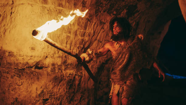 istock Primeval Caveman Wearing Animal Skin Exploring Cave At Night, Holding Torch with Fire Looking at Drawings on the Walls at Night. Neanderthal Searching Safe Place to Spend the Night 1194512821