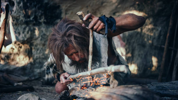 nahaufnahme eines urhöhlenmenschen, der tierhaut trägt und versucht, feuer mit bogenbohrmethode zu machen. neandertaler kindle erste mann-made feuer in der geschichte der menschlichen zivilisation. making fire für kochen. - animal skin stock-fotos und bilder