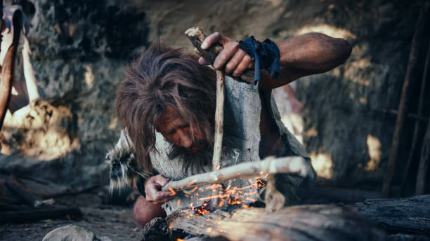 close-up shot of a primeval caveman wearing animal skin trying to make fire with bow drill method. neanderthal kindle first man-made fire in the human civilization history. making fire for cooking. - neanderthal imagens e fotografias de stock