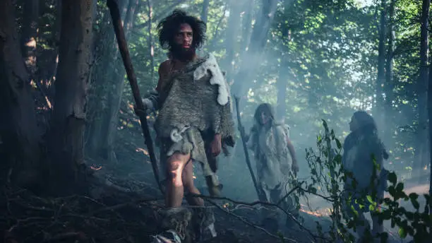 Tribe of Hunter-Gatherers Wearing Animal Skin Holding Stone Tipped Tools, Explore Prehistoric Forest in a Hunt for Animal Prey. Neanderthal Family Hunting in the Jungle or Migrating for Better Land