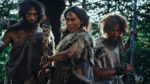 female leader and two primeval cavemen warriors threat enemy with stone tipped spear, scream, defending their cave and territory in the prehistoric times. neanderthals / homo sapiens tribe - neanderthal imagens e fotografias de stock