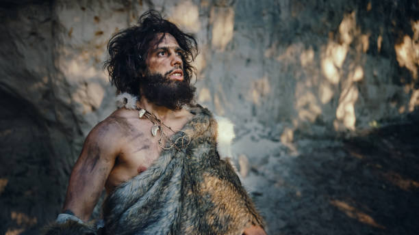portrait of primeval caveman wearing animal skin looks around forest defending his cave and territory in the prehistoric times. prehistoric neanderthal or homo sapiens leader - neanderthal imagens e fotografias de stock