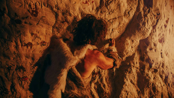 Primitive Prehistoric Neanderthal Wearing Animal Skin Draws Animals and Abstracts on the Walls at Night. Creating First Cave Art with Petroglyphs Rock Paintings Illuminated by Fire. Back View la piel de animal de ropa de animal de mal estado de neanderthal prehistoric dibuja animales y resúmenes en las paredes por la noche. creación de primer arte rupestre con petroglifos pinturas rupestres iluminadas por el fuego. vista posterior