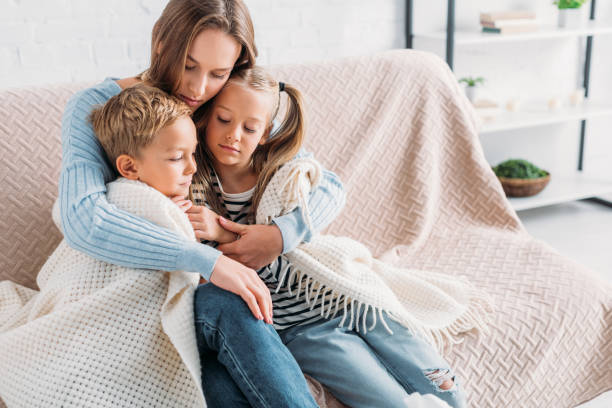 caring mother wrapping sick children in blanket while sitting on sofa caring mother wrapping sick children in blanket while sitting on sofa single mother stock pictures, royalty-free photos & images