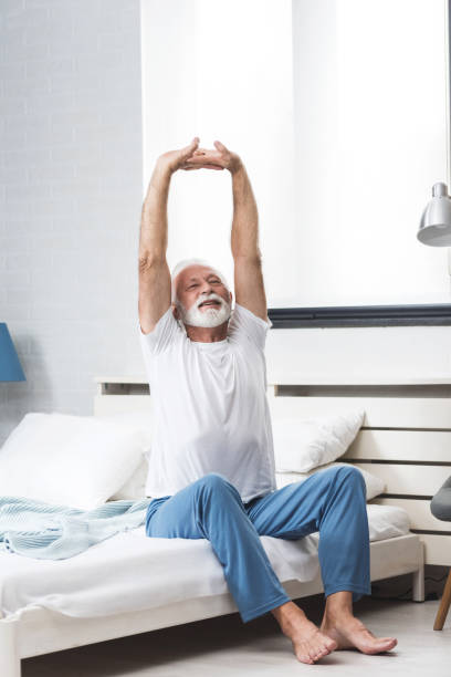 Senior man stretch on bed in morning Portrait of a senior  man in pajamas waking up in bed and stretching his arms. Concept of energy from the early morning of a single retired man old man pajamas photos stock pictures, royalty-free photos & images