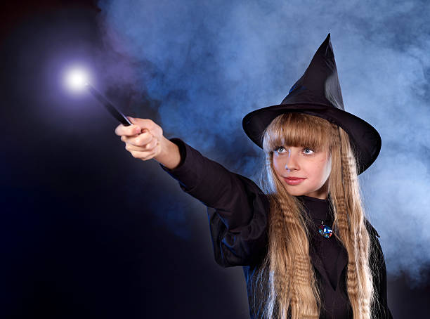 Girl in witch's hat with magic wand. stock photo