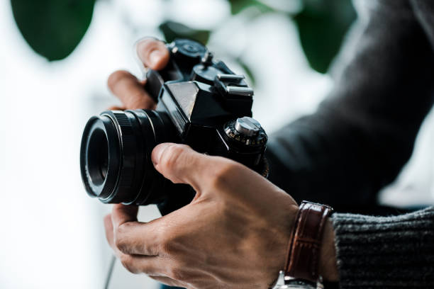vista recortada de hombre bi-racial sosteniendo la cámara digital en apartamento - fotógrafo fotografías e imágenes de stock