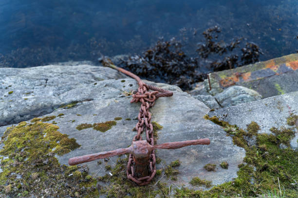 istock rusty purple anchor chain on a mossy stone leading into the dark water with algae in Norway, Alesund 1194534207