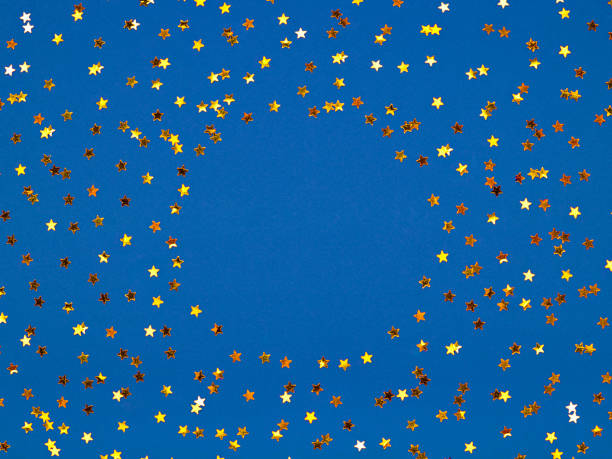 Classic blue background covered with golden stars sequins. Top view. Copy space for text. Christmas time frame. Concept of winter holiday.