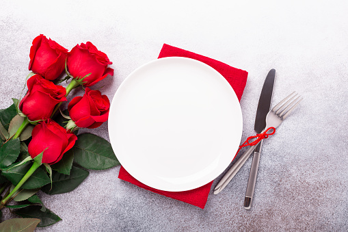 Valentines day table place setting with bouquet of red roses and silverware on stone background. Top view. Valentine's card - Image