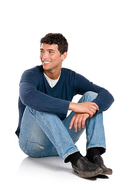 Smiling young man, looking away from the camera Smiling young man looking away with embarassement isolated on white background. sitting on floor stock pictures, royalty-free photos & images