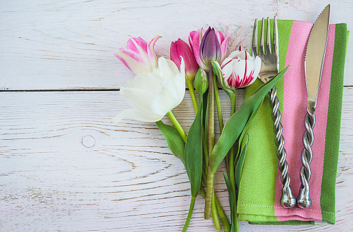 Fork and knife on the green napkin and bouquet of red tulips on the old non paint wooden background. Copy space, flat lay
