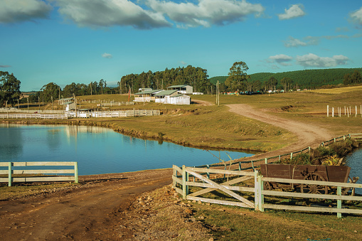 Pretty farm with fences, livestock sheds and blue lake on landscape of rural lowlands called Pampas at Cambara do Sul. A small country town in southern Brazil with amazing natural tourist attractions.