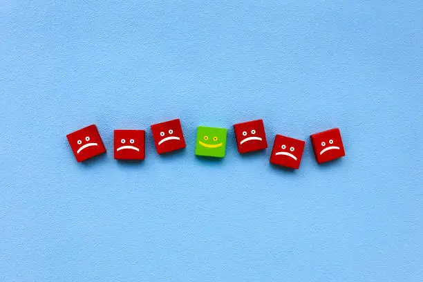 Photo of Happy and sad face emojis on wood blocks toys and blue background