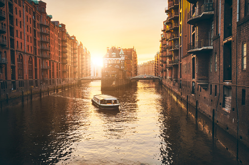 Hamburg warehouse district in golgen hour sunset lit. Water castle palace and tourist visting boat trip in river. Old warehouse port, Germany, Europe
