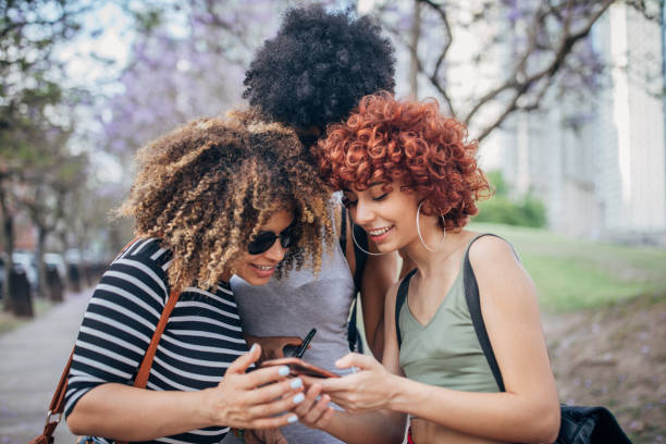 istock Three young women using phone outdoors 1194551603