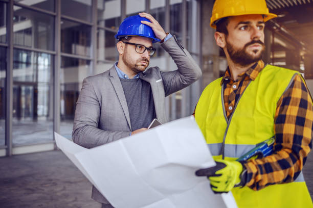 istock Upset architect holding his head and thinking about mistake he made on blueprints. Construction worker holding blueprints and looking away. 1194554157