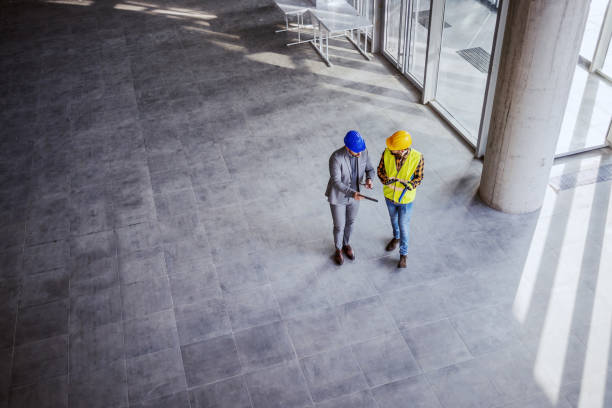 vista superiore dell'architetto che tiene tablet e parla con l'operaio edile di nuove idee sul progetto su cui stanno lavorando. costruzione in costruzione interno. - construction construction worker architect business foto e immagini stock