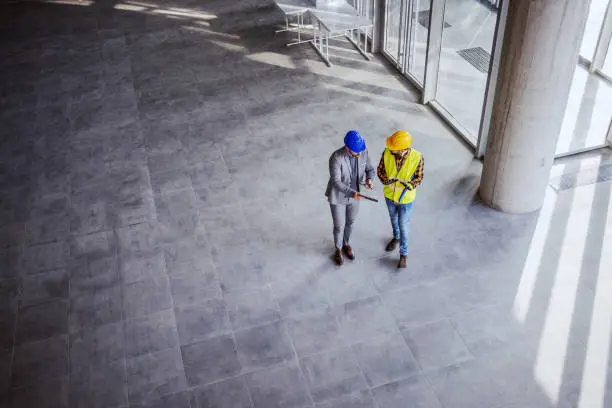 Photo of Top view of architect holding tablet and talking with construction worker about new ideas on project they working on. Building in construction process interior.