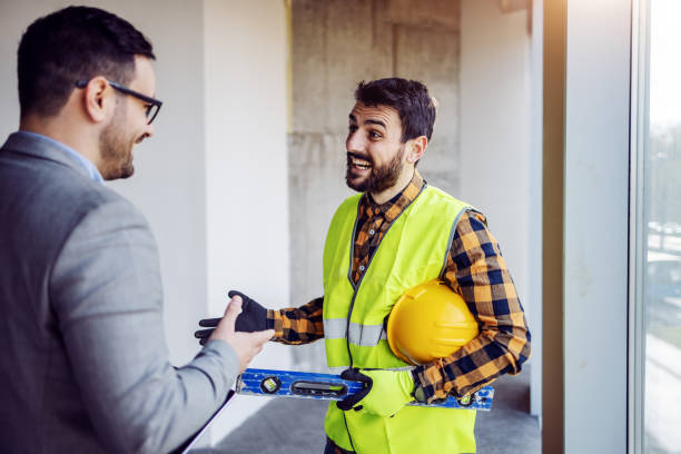 istock Handsome Caucasian bearded construction worker in work wear talking with his boss about project. Building in construction process interior. 1194556181