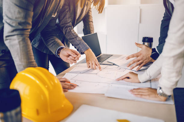 istock Group of dedicated hardworking highly motivates architects looking and pointing at blueprints on desk inside of building they want to renew. 1194556536