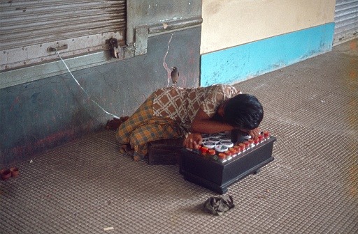 Madhya Pradesh, India, 1975. A Shoe cleaner in India is taking a nap. His bird, tied to a string, watches over the sleeping shoe cleaner.